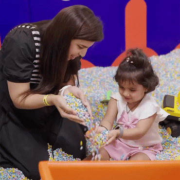 Child exploring colourful sensory balls with an adult at Wooray Hyderabad play area.